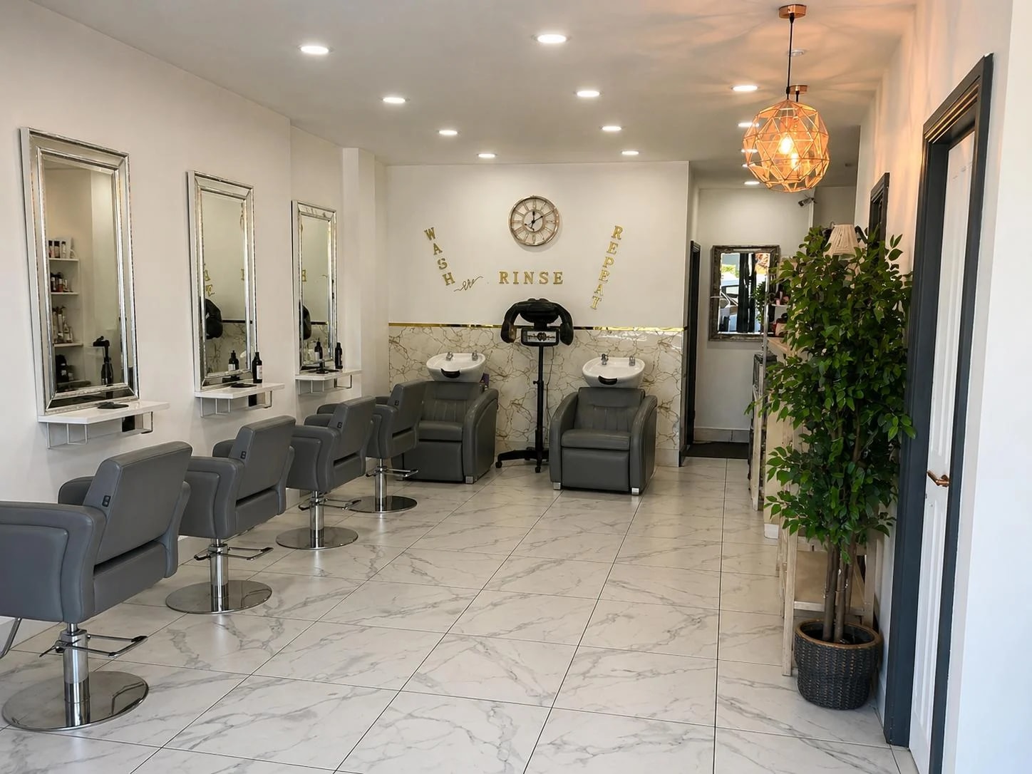 Inside The Essentials Lounge, with mirrors, grey salon chairs and warm pendant lighting