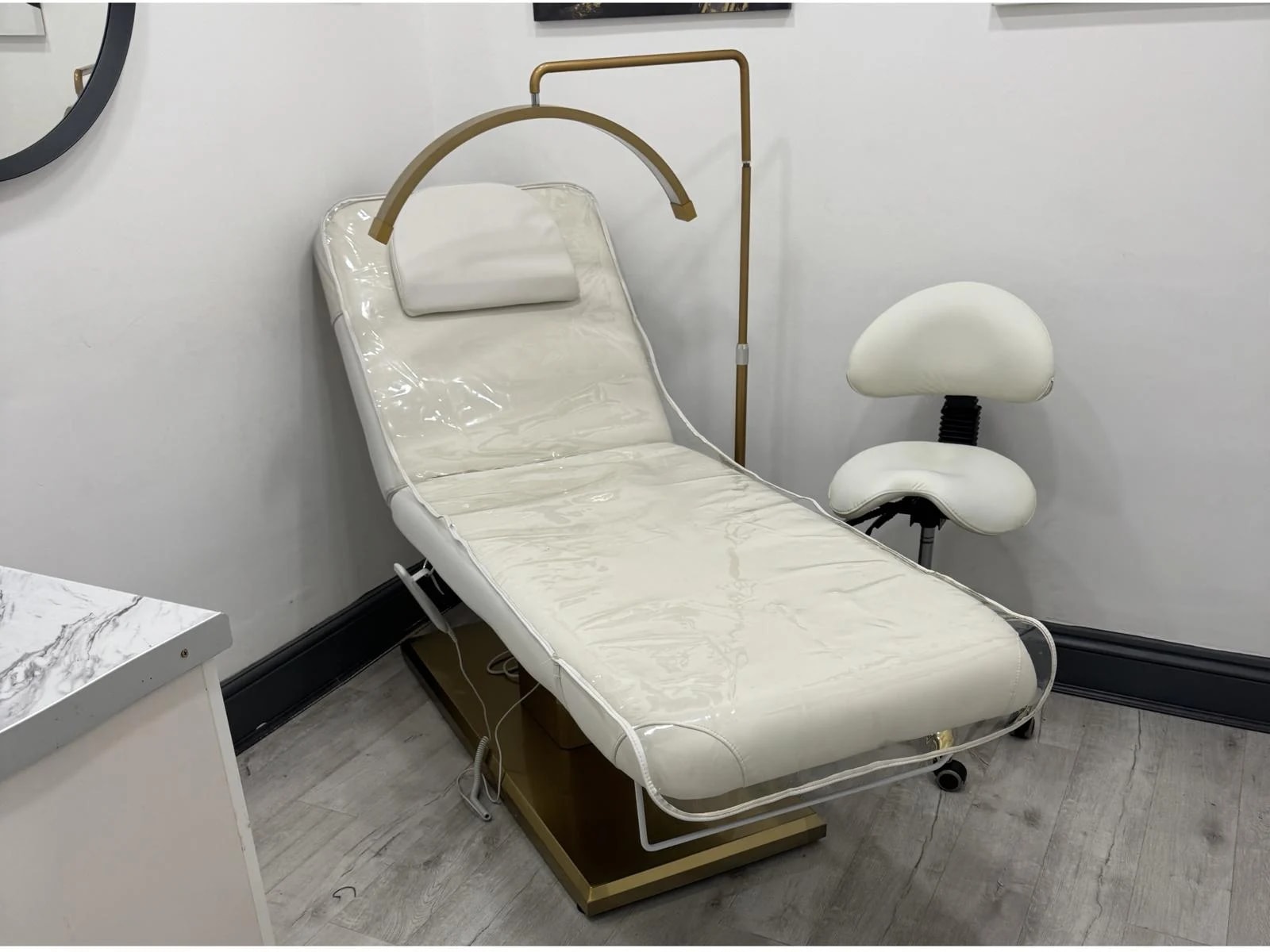 Treatment room with an ivory treatment couch, gold lamp and practitioner stool